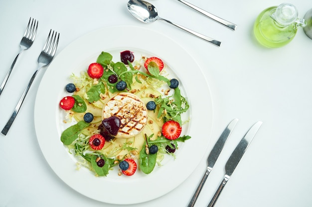 Gegrilde camembertkaas met appels, aardbeien en bosbessen in een witte plaat op een witte plaat