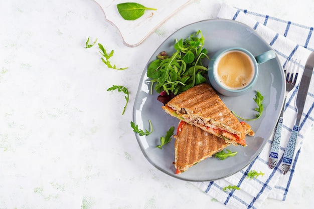 Gegrilde clubsandwich panini met rundvlees, tomaat, kaas, sla en kopje koffie