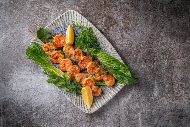 Gegrilde gamba's met citroen en kruiden op een bord tegen een grijze stenen tafel, viskebab