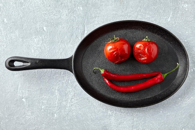 Gegrilde gebakken tomaten en roodgloeiende pepers in de vorm van een smiley in een zwarte gietijzeren pan