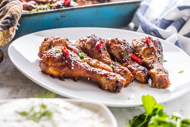 Gegrilde geroosterde en barbecue kippenpoten op wit bord met kruidendecoratie.