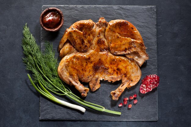 Foto gegrilde geroosterde kip tabaka op een zwart stenen bord