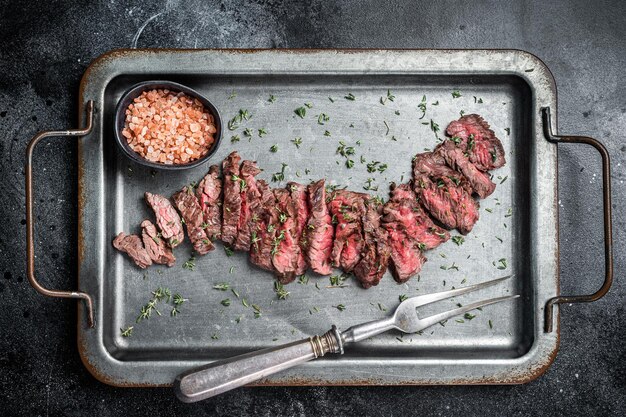 Gegrilde gesneden Machete beef steak op stalen dienblad met tijm zwarte achtergrond bovenaanzicht