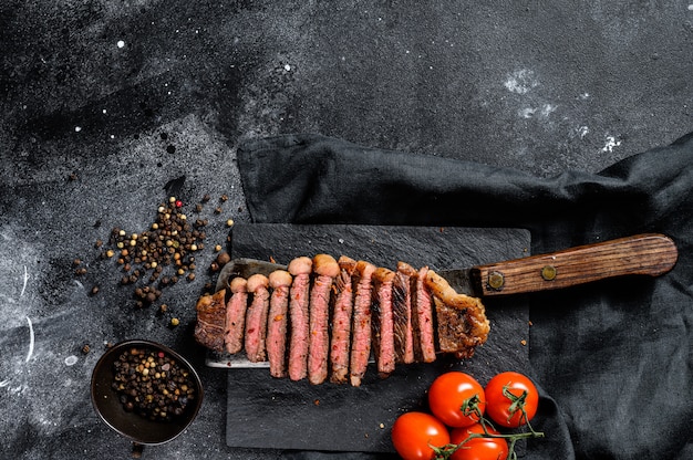 Gegrilde gesneden strip loin steak op een hakmes. Zwart oppervlak. Bovenaanzicht. Kopieer ruimte