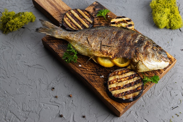 Gegrilde gevulde dorado vis met citroenkruiden en aubergine op een houten plank