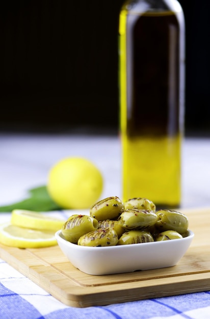 Gegrilde groene olijven met rozemarijn, olijfolie en citroen in een bord op houten snijplank op tafel