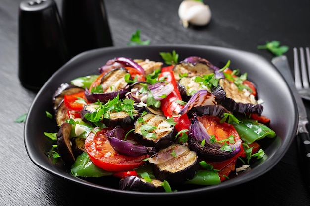 Gegrilde groenten aubergine paprika courgette rode ui tomaat met knoflook op een zwarte plaat