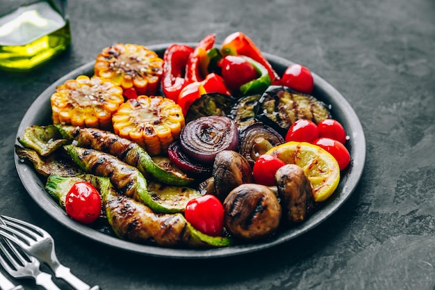 Gegrilde groenten in kom op donkere stenen ondergrond Courgette paprika, zoete maïs, tomaten, rode uien en aubergine