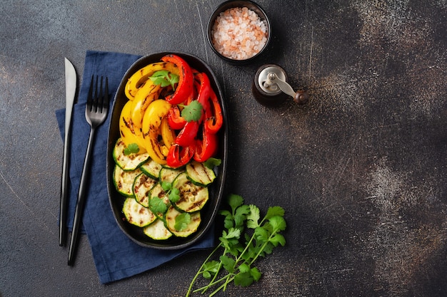 Gegrilde groenten stukjes courgette, rode en gele peper en een boeket koriander op plaat, salade op bbq grillrek boven houtskool. Bovenaanzicht. Barbecue concept