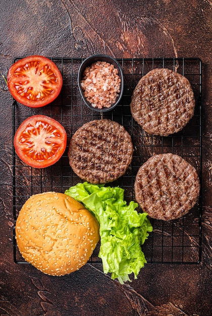 Gegrilde hamburgerpasteitjes met tomaten en kruiden op keukentafel donkere achtergrond bovenaanzicht