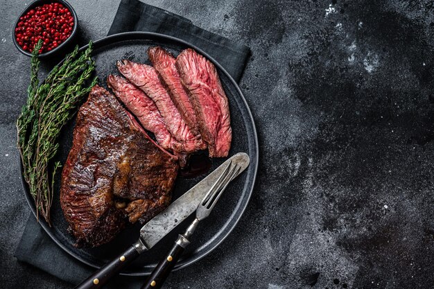 Gegrilde hanger of Onglet beef steak op een bord met tijm. Zwarte achtergrond. Bovenaanzicht. Ruimte kopiëren.