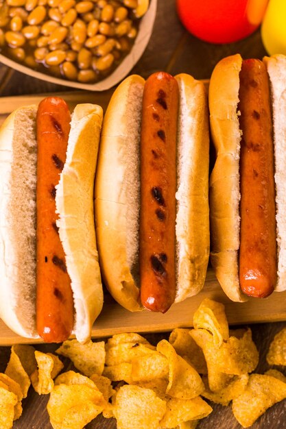 Gegrilde hotdogs op een witte hotdogbroodjes met chips en gebakken bonen aan de zijkant.