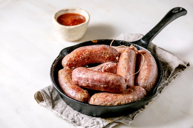 Gegrilde italiaanse worst salsiccia in gietijzeren pan op doek servet over witte marmeren tafel. plat leggen, ruimte