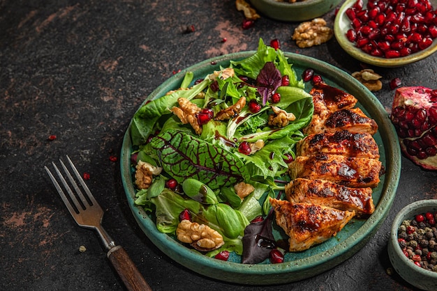 Gegrilde kipfilet en mix salade met walnoten granaatappel en balsamico saus in een bord met vork op zwarte tafel gezonde voeding