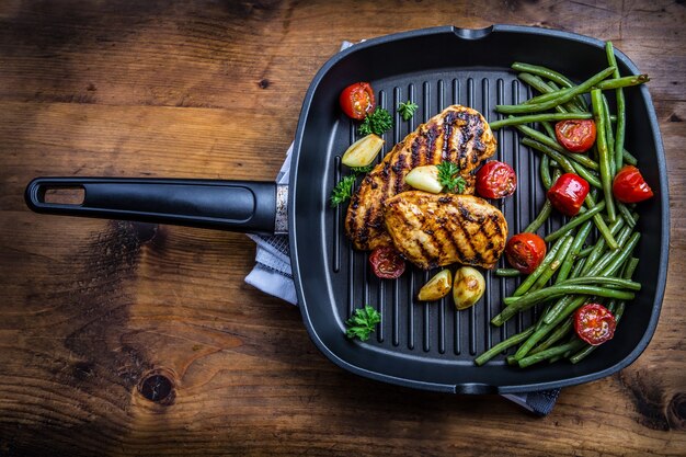 Gegrilde kipfilet in verschillende variaties met cherrytomaatjes, sperziebonen, knoflookkruiden gesneden citroen op een houten plank of teflon pan