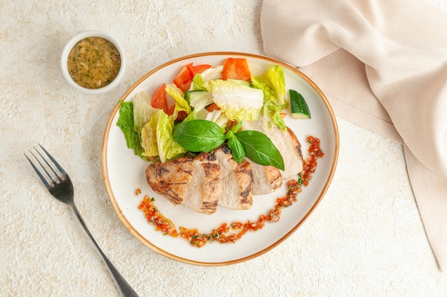Gegrilde kipfilet met groenten op een bord. Ernaast staat een juskom met Bearnaisesaus, een vork en een beige servet. Lichte achtergrond. Uitzicht van boven.