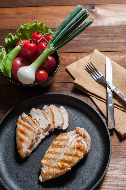 Gegrilde kipfilet op pan. Rauwe groenten in kom, houten achtergrond