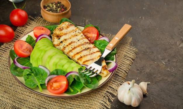 Gegrilde kippenborst en verse groentesalade met spinazie, avocado en tomaten op een donkere tafel. Gezonde levensstijl. Ketogeen dieet. Het concept van dieetvoeding. Kopieer ruimte