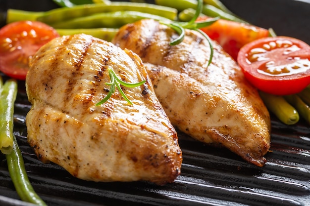 Gegrilde kippenborsten op een grillpan met verse groene groente en cherrytomaatjes en rozemarijntakjes.