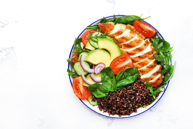 Gegrilde kippenvlees rode quinoa en verse groentesalade met tomaat, avocado en spinazie Gezonde detox ketogene dieetvoeding Witte achtergrond bovenaanzicht