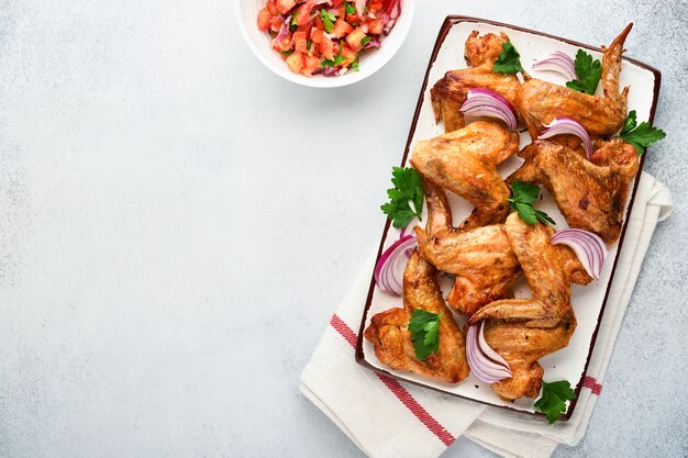 Gegrilde kippenvleugels of geroosterde bbq met kruiden en tomatensalsasaus op plaat op een lichtgrijze leisteen, steen of betonnen ondergrond. bovenaanzicht met kopie ruimte.