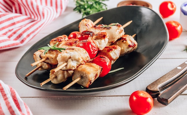 Gegrilde kipspiesjes met kerstomaatjes op zwarte plaat Witte houten tafel Selectieve aandacht