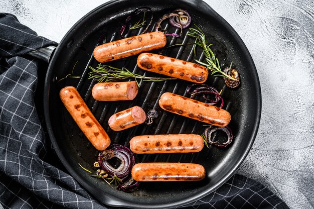 Gegrilde klassieke varkensworstjes met ui, knoflook en rozemarijn in een pan.