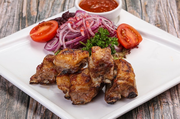 Gegrilde lamsribbetjes met tomatensaus geserveerd met uienringen