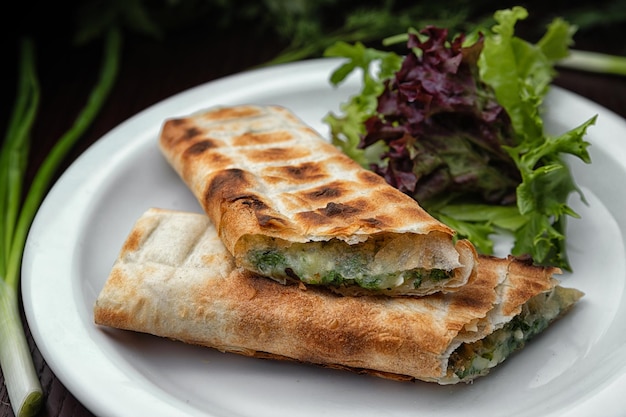 Gegrilde lavash met suluguni-kaas op een bord met groene uien en sla met selectieve focus