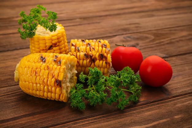 Gegrilde maïskolven met tomaten en peterselie op houten ondergrond