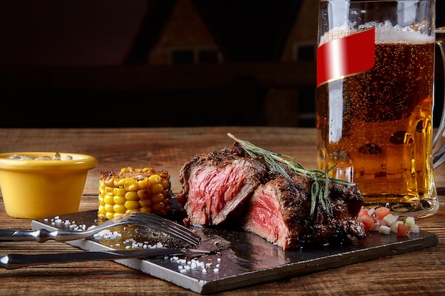 Gegrilde ossenhaasbiefstuk rosbief en champignonsaus op zwarte snijplank en glas bier op w...