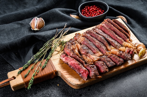 Gegrilde rib eye, ribeye steak op een snijplank, medium rood. gemarmerd vlees. zwarte achtergrond. bovenaanzicht