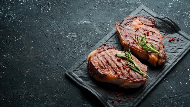 Gegrilde ribeye-biefstuk met kruiden op een zwarte stenen tafel Bovenaanzicht Vrije ruimte voor uw tekst