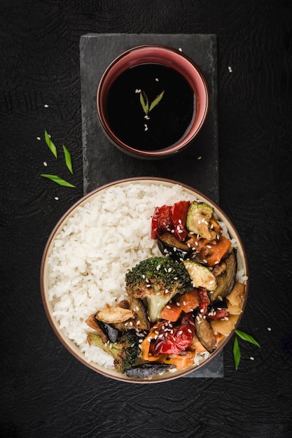 Gegrilde rijst en groentenkom met sojasaus op een zwart grafietbord op een donkere achtergrond. Aziatisch eten. Verticale oriëntatie. Bovenaanzicht.