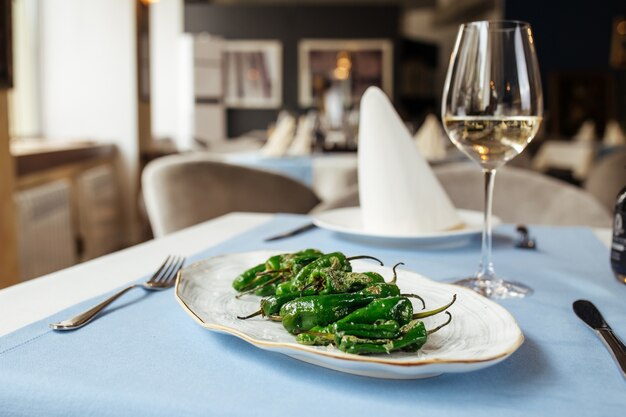 Gegrilde Spaanse groene padron paprika's op de blauwe tafel met witte wijn