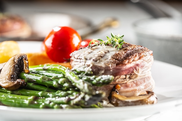 Gegrilde steak met spek geserveerd op een bord met asperges, champignons en tomaat.