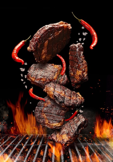 Gegrilde steaks van varkensvlees of rundvlees met chili en zout vallen op zwarte achtergrond barbecue grill...
