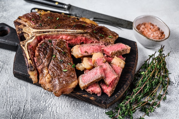 Gegrilde T-bone rundvlees biefstuk gesneden op een houten snijplank op witte tafel. Bovenaanzicht.