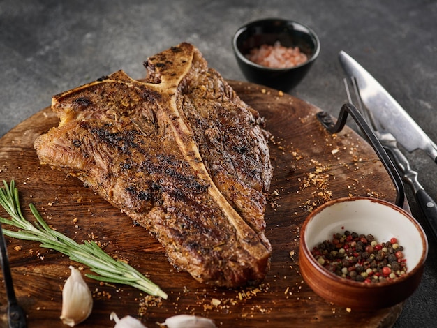 Gegrilde tbone steak met zout en peper op snijplank op donkergrijze achtergrond