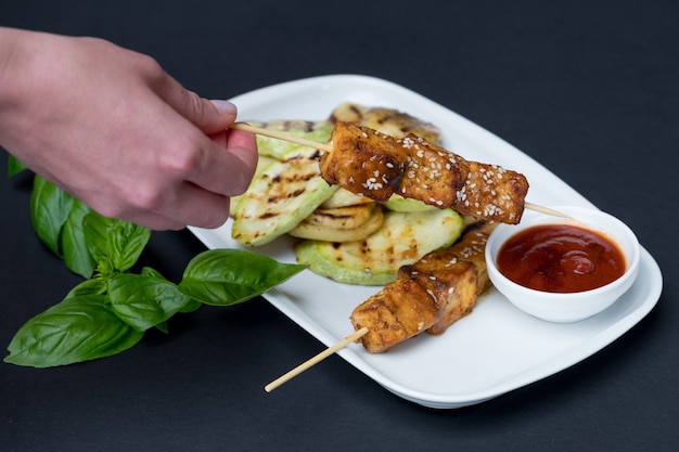 Gegrilde tofu-kebab op een witte plaat. Zwarte achtergrond. Verse basilicumblaadjes.