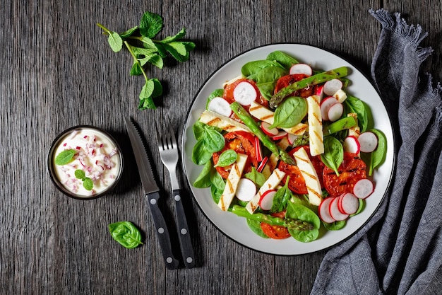 Gegrilde tomaten, Halloumi-kaas, asperges, radijs en spinaziesalade op een bord op een houten tafel, horizontaal zicht van bovenaf, plat gelegd, vrije ruimte