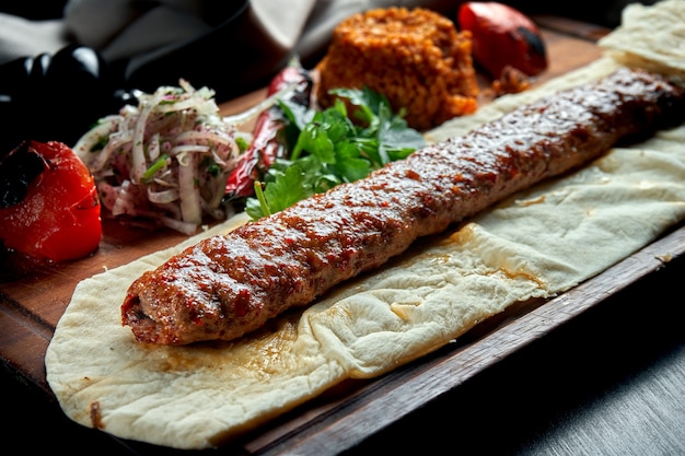 Gegrilde Turkse lam lula kebab met gegrilde groenten, ui en rijst op een houten bord