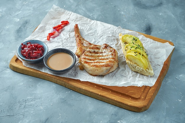 Gegrilde varkenslapje vlees met sauzen en croutons op een houten bord. Varkenshaas