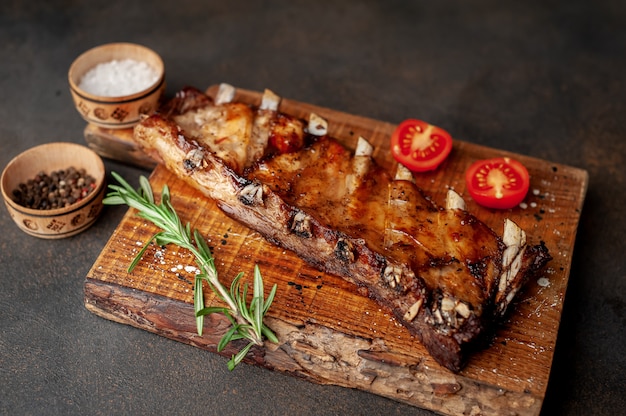 gegrilde varkensribbetjes op een snijplank met kruiden op een stenen achtergrond