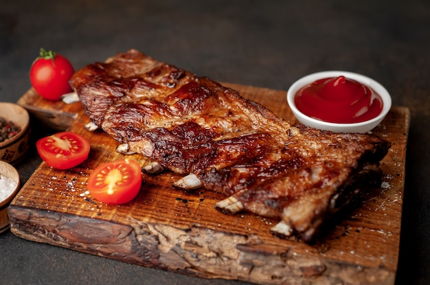 gegrilde varkensribbetjes op een snijplank met kruiden op een stenen achtergrond