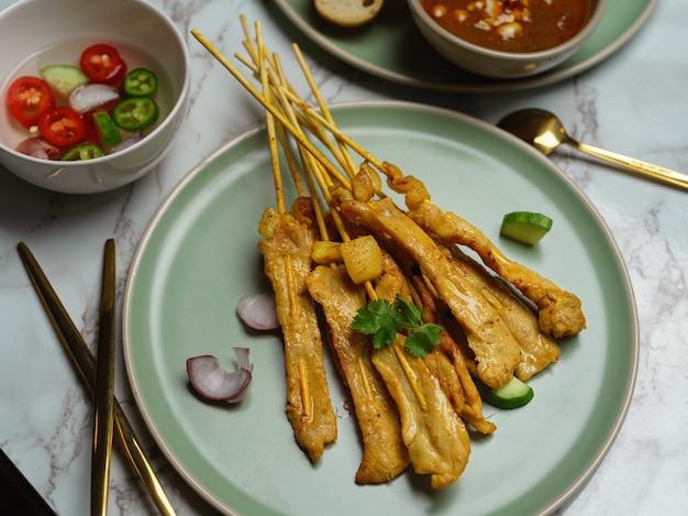 Gegrilde varkenssaté (Moo Satay) met komkommer en ui geserveerd met pindasaus en bijgerecht