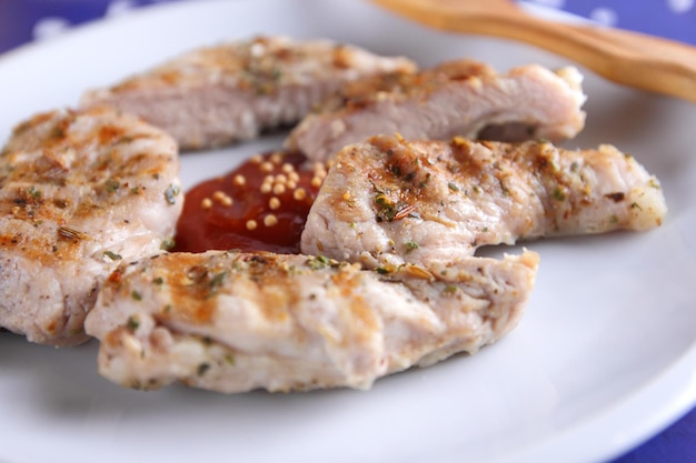 Gegrilde varkenssteak met kruiden op een tafel Varkenssteak met houten vork en tomatensaus op een witte plaat Close-up