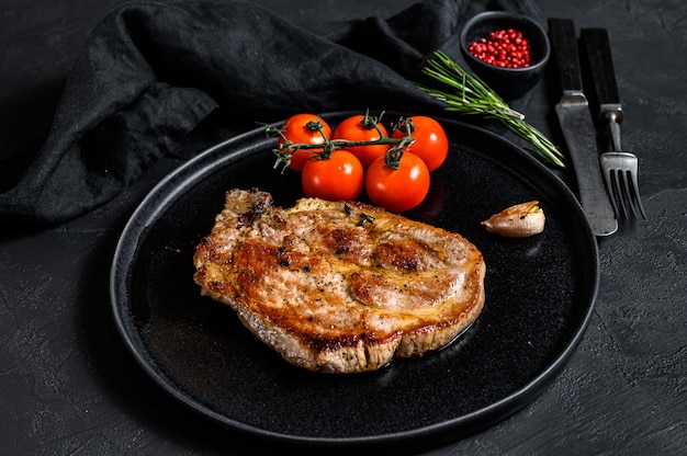 Gegrilde varkensvlees steak op bot met tomaten. Zwarte achtergrond. Bovenaanzicht