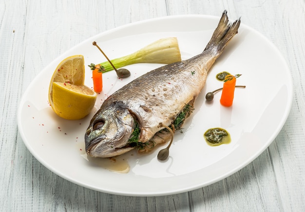 Gegrilde vis op schotel geïsoleerd op wit. Bovenaanzicht van hele geroosterde dorado