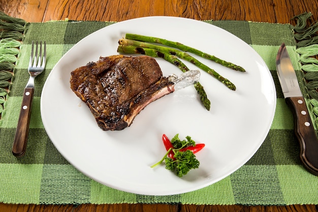 Gegrilde vleesribben op een witte plaat met tomaten bieslook en donkere hete saus aan boord